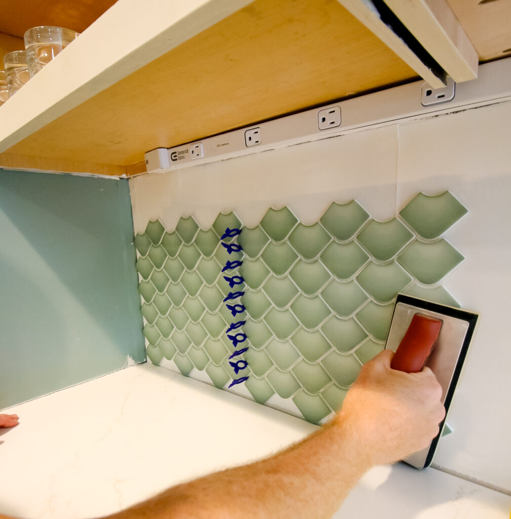 pressing cutting musselbound peel and stick adhesive sheets into the wall with a grout float