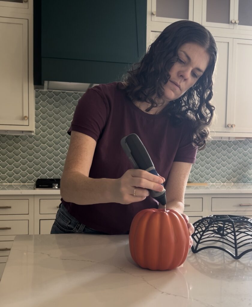 applying hot glue to the top of a faux pumpkin