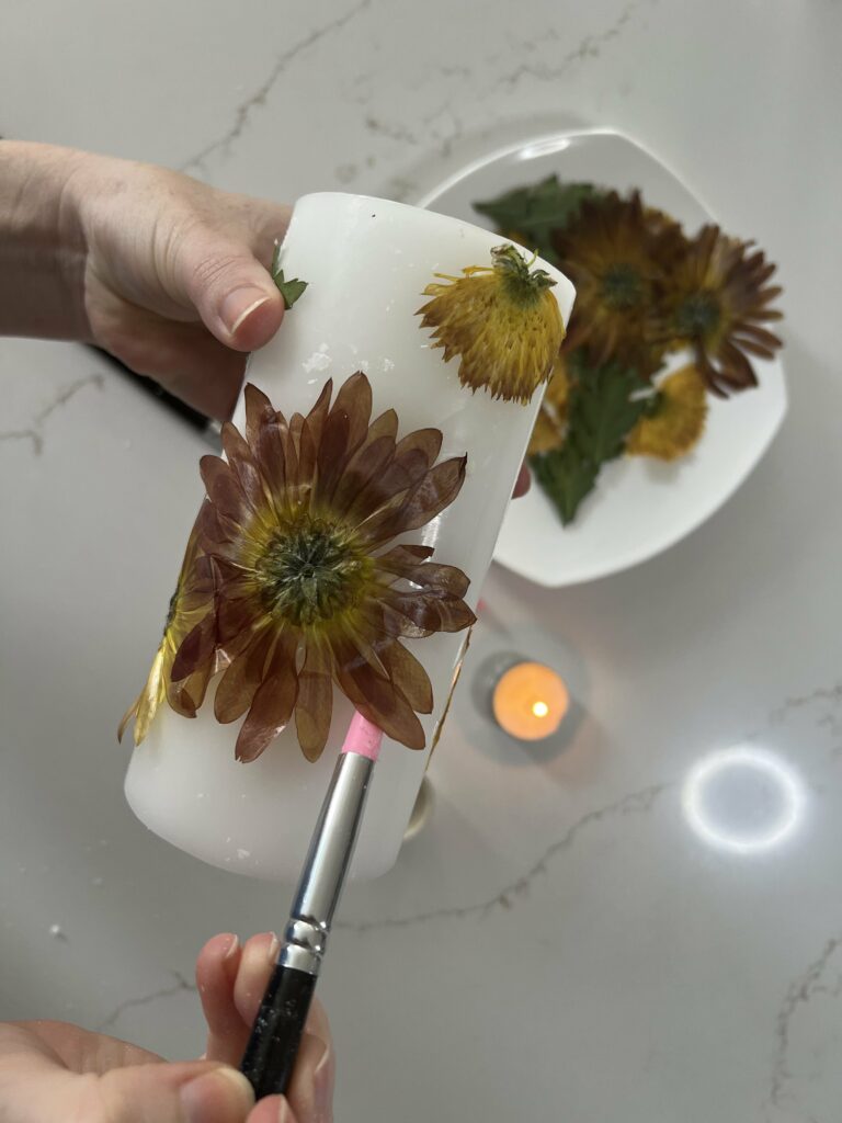 attaching dried flowers to a candle with wax