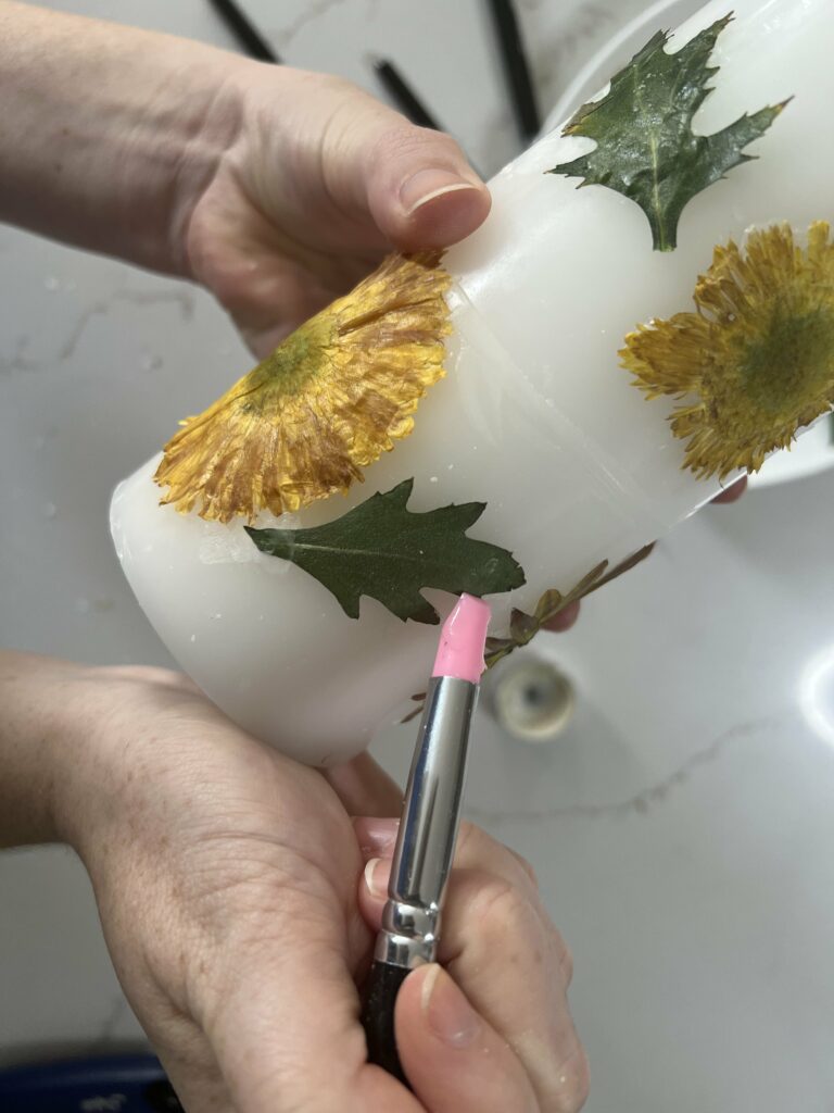 attaching dried flowers to a candle with wax