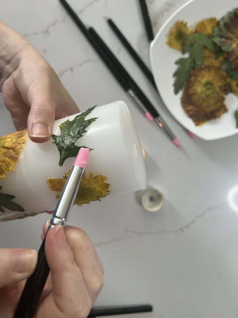 attaching dried flowers to a candle with wax